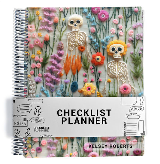 The image is a colorful spiral-bound planner with a floral and skeleton design. The cover features a variety of flowers and skeletal figures, creating a visually appealing and unique design.