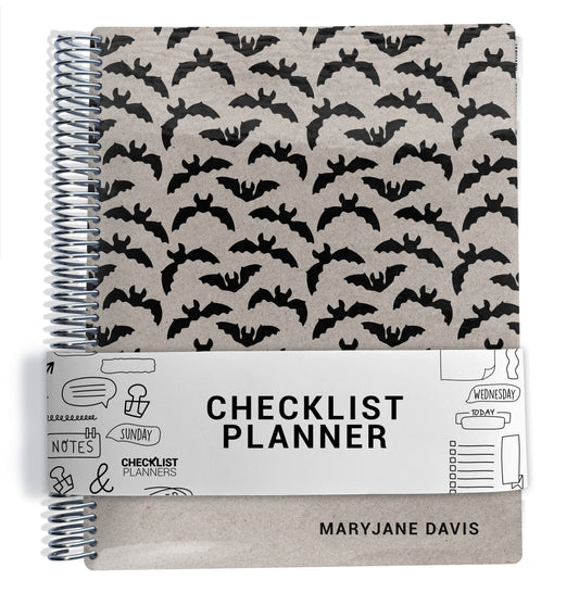 a spiral-bound notebook with a black bat pattern on the cover and a white label that reads "CHECKLIST PLANNER" in bold black letters.